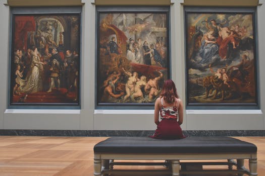 jeune femme assise sur un banc regardant des tableaux dans un musée