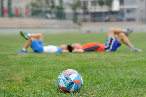 deux jeunes allongés dans l'herbe et un ballon de foot au premier plan
