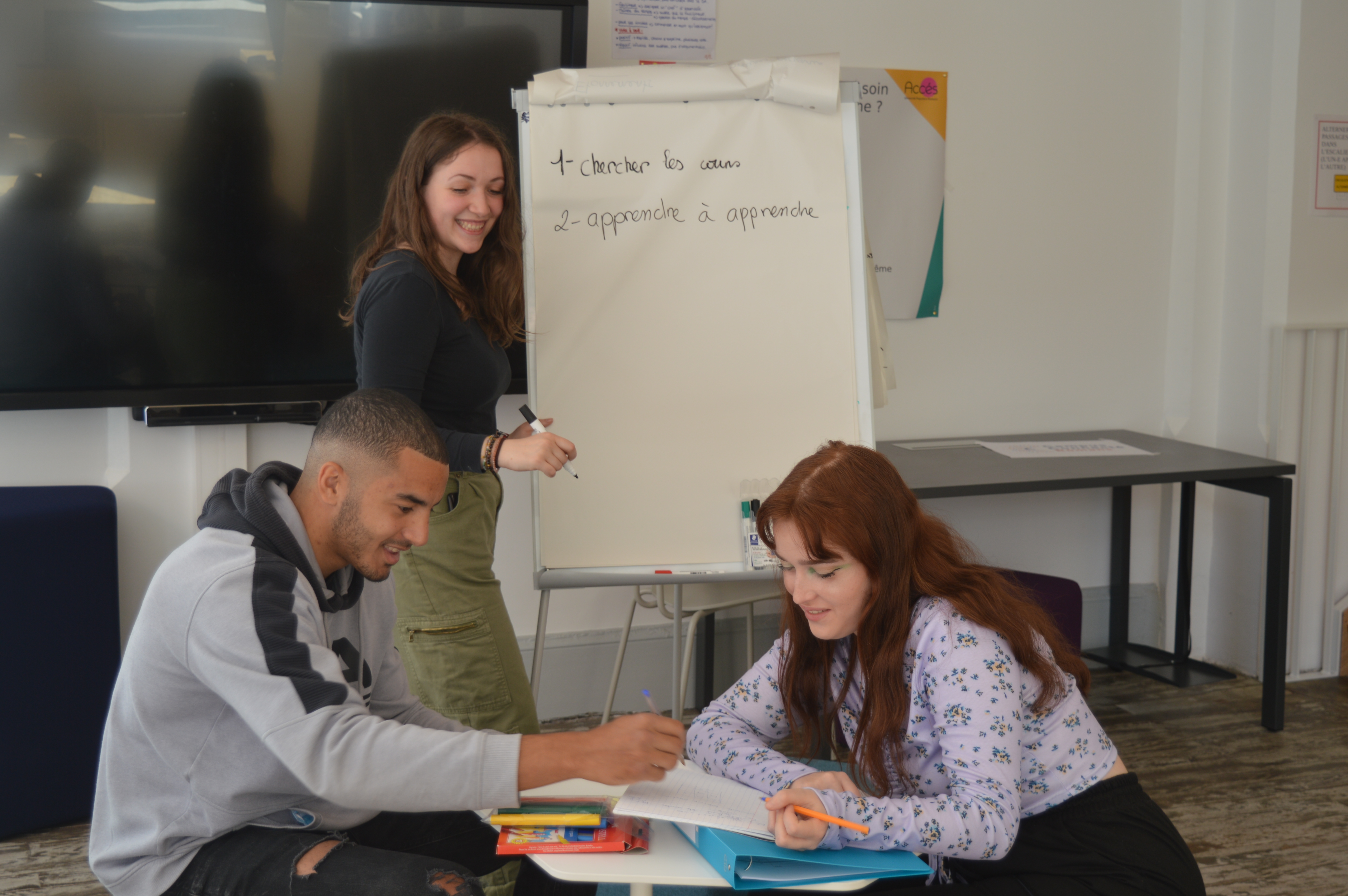 un jeune homme et deux jeunes filles échangeant et écrivant sur un paperboard